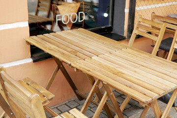 Folding tables and chairs made of wooden slats. Summer cafe on the sidewalk of the street.