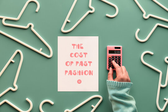 The cost of fast fashion. Plastic hangers, hand with calculator and page with text. Creative top view flat lay on green background.