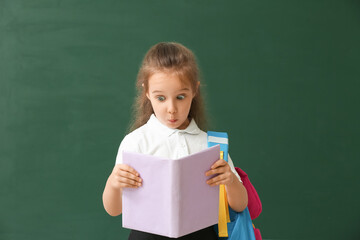 Surprised little schoolgirl with book on color background