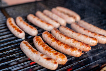 Sausages on grill, with smoke above it.Pork sausages grilling on a portable BBQ with one sausage being turned in a pair of tongs on a summer picnic, close up of the grill, meat and fire