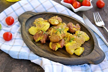 Crash Hot Potatoes, boiled potatoes in a peel, crushed and baked with olive oil and herbs on a wooden plate on a dark concrete background. Australian cuisine. Potato recipes.