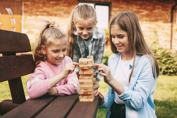 Three girlfriends play a wooden board game outdoors near their house.