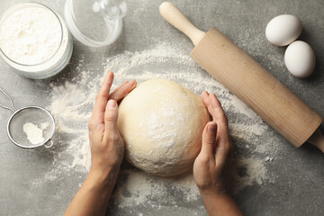 Female hands hold dough on gray background with ingredients for baking
