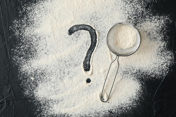 Flour, sieve and question mark on black background