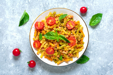 Fusilli - classic italian pasta from durum wheat with chicken meat, tomatoes cherry, basil in tomato sauce in white bowl on gray concrete table Mediterranean cuisine Top view Flat lay
