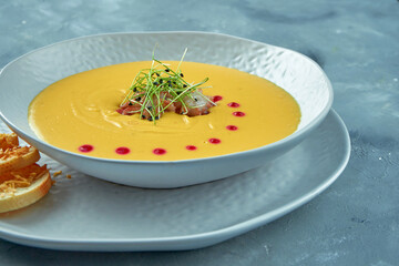 Pumpkin cream soup with octopus and croutons in a white bowl on a gray background. Creamy seafood soup