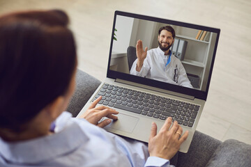 Fototapeta na wymiar Smiling confident man doctor greeting man patient with hand online from laptop