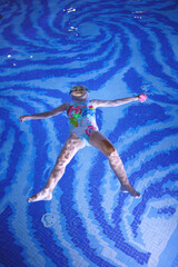 little girl in a pool cap and blue swimsuit learns to swim in the pool