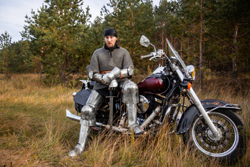 A medieval warrior in armor sits on a motorcycle with a sword in his hands on the background of the...