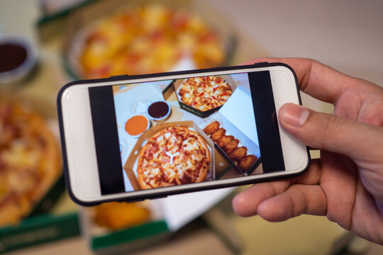 Woman's hand is focused on taking a picture of a pizza on a smartphone for loading in social networks. The concept of using a mobile phone, taking pictures