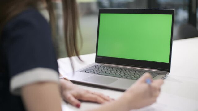 Over the shoulder shot of business woman who is studying remotely looking at green screen. Office person using laptop computer with laptop green screen.