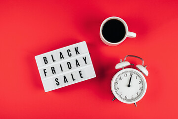 Black friday sale word on lightbox, cup of coffee, alarm on red background table. Flat lay