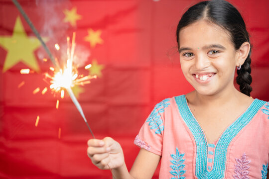 Smiling Young Girl Kid Holding Sparkler In Hand With Chinese Flag As Background - Concept Showing Celebration Of Chinas National Or Republic Day