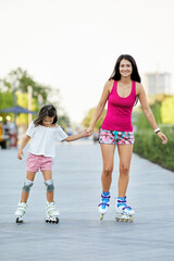 Young mother and her little daughter rollerskating in park