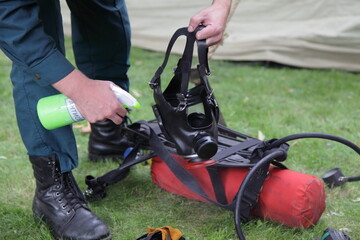 Rescuer man is treated with an antibacterial spray to gas mask on rescue tent and green grass...