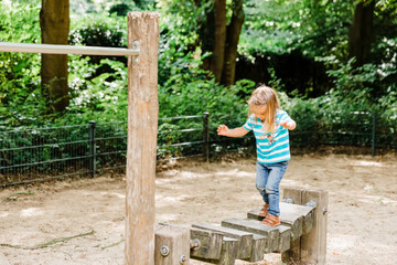 Toddler girl walking on wooden playground equipment
