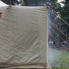 Canvas military tent with smoke, rescuer firefighter training site in Park on summer day