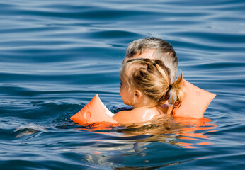 Grandfather holding toddler girl with floaters in sea