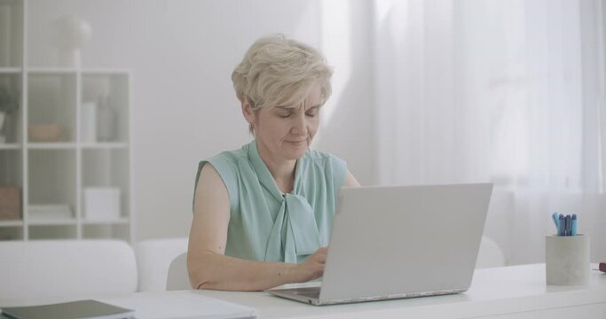 aged woman is working with laptop in home, feeling sharp toothache, touching cheek and grimacing by pain