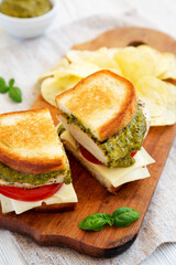 Homemade Pesto Chicken Sandwich with Potato Chips on a rustic wooden board, side view. Close-up.