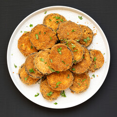 Homemade Garlic Parmesan Baked Eggplant on a plate on a black surface, top view. Overhead, from above, flat lay.