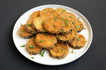 Homemade Garlic Parmesan Baked Eggplant on a plate on a black background, low angle view.