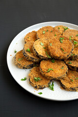 Homemade Garlic Parmesan Baked Eggplant on a plate on a black surface, side view. Close-up.