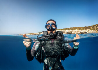 Underwater split view of a female scuba diver on the surface showing the OK sign with her hands