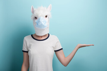 Young woman wearing alpaca and protection medical mask, hold hand with open palm and empty space...