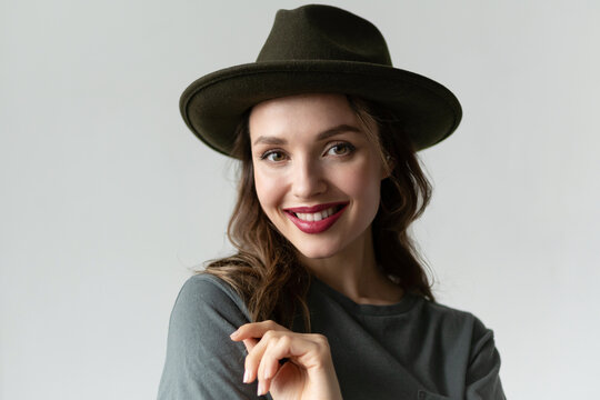 Close up portrait of young smiling millenial woman wearing stylish black hat and looking at camera in studio isolated on gray background. Trendy autumn accessories. Perfect smile and body language