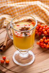 Hot sea buckthorn tea with brown sugar, cinnamon, carnation in glass cup on wooden background