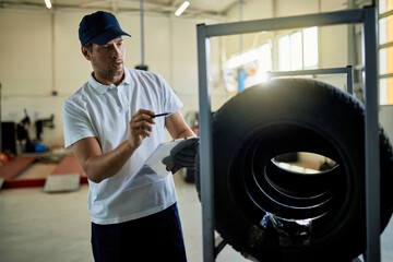 Mid adult  mechanic checking stack of car tires in auto repair shop.