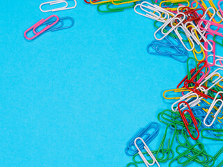 Colored paper clips on blue background with copyspace