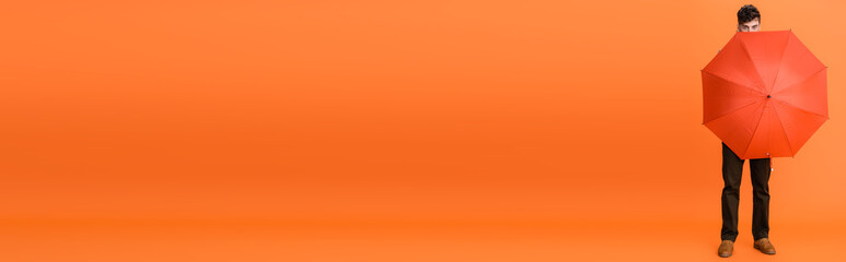 full length of man in brown pants holding umbrella on orange, panoramic shot © LIGHTFIELD STUDIOS