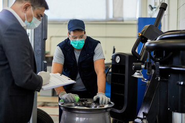 Auto mechanic and his manager wearing protective masks while working in auto repair shop.