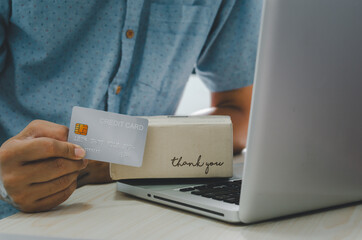 Man hands are holding a credit card and a box parcel hematite and laptop at the table.Online delivery service business concept.