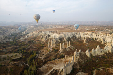 Fototapeta na wymiar Colorful hot air balloon ride and tour in Goreme valley, semi-arid region in central Turkey known for its distinctive fairy chimneys, tall, cone-shaped rock formation- Cappadocia, Turkey