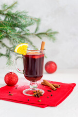 Mulled wine with cinnamon, anise, cloves and orange in a mug on the background of a Christmas tree.