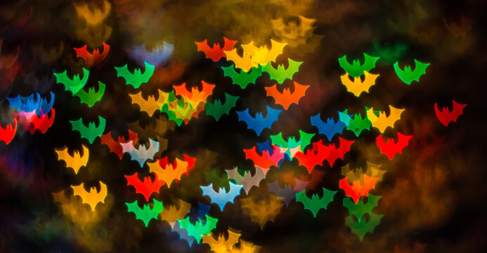 Abstract background for Halloween, bokeh in the form of bats in red, yellow, blue, green and orange on a dark background. Space for text - Powered by Adobe