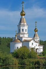 Fototapeta na wymiar Above a small river stands an Orthodox Church against a blue sky with white clouds