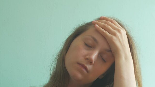Stressed brown hair woman with headache on pastel mint background. Tired young lady without make-up feel pain, massaging temples. Hard to wake up, morning concept. PMS premenstrual syndrome problems.