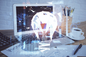 Computer on desktop in office with bulb icon hologram. Double exposure. Concept of idea.