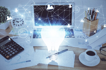 Computer on desktop in office with bulb icon hologram. Double exposure. Concept of idea.