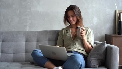 Happy young woman relaxing on sofa with computer, chatting with friends online in social network, answering messages emails, web surfing information, shopping in internet store in cozy studio home - Powered by Adobe