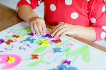 Little toddler girl playing with different colorful stickers and painting flowers. Concept of activity of children during pandemic corona virus quarantine. Child learning colors with parents at home