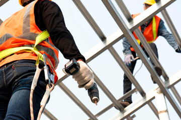 Construction workers wear safety straps while working on the building's roof structure at a...