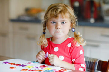 Little toddler girl playing with different colorful stickers and painting flowers. Concept of activity of children during pandemic corona virus quarantine. Child learning colors with parents at home