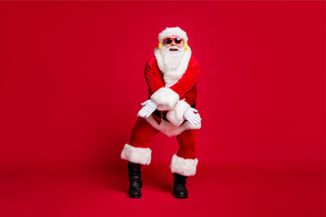 Full length photo of pensioner old man grey beard retro dance night club wear santa x-mas costume gloves coat belt sunglass headwear earphones black boots isolated red color background