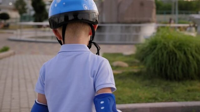 A little boy in a blue helmet and elbow pads rides a gyro scooter or Segway in a circle in the Park.