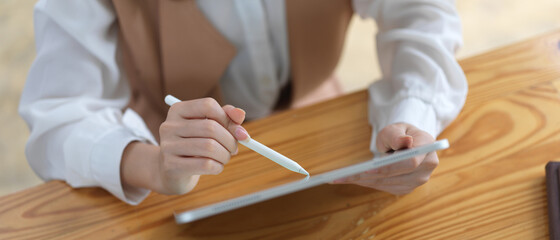 Cropped shot of female hands using digital tablet with stylus on wooden table
